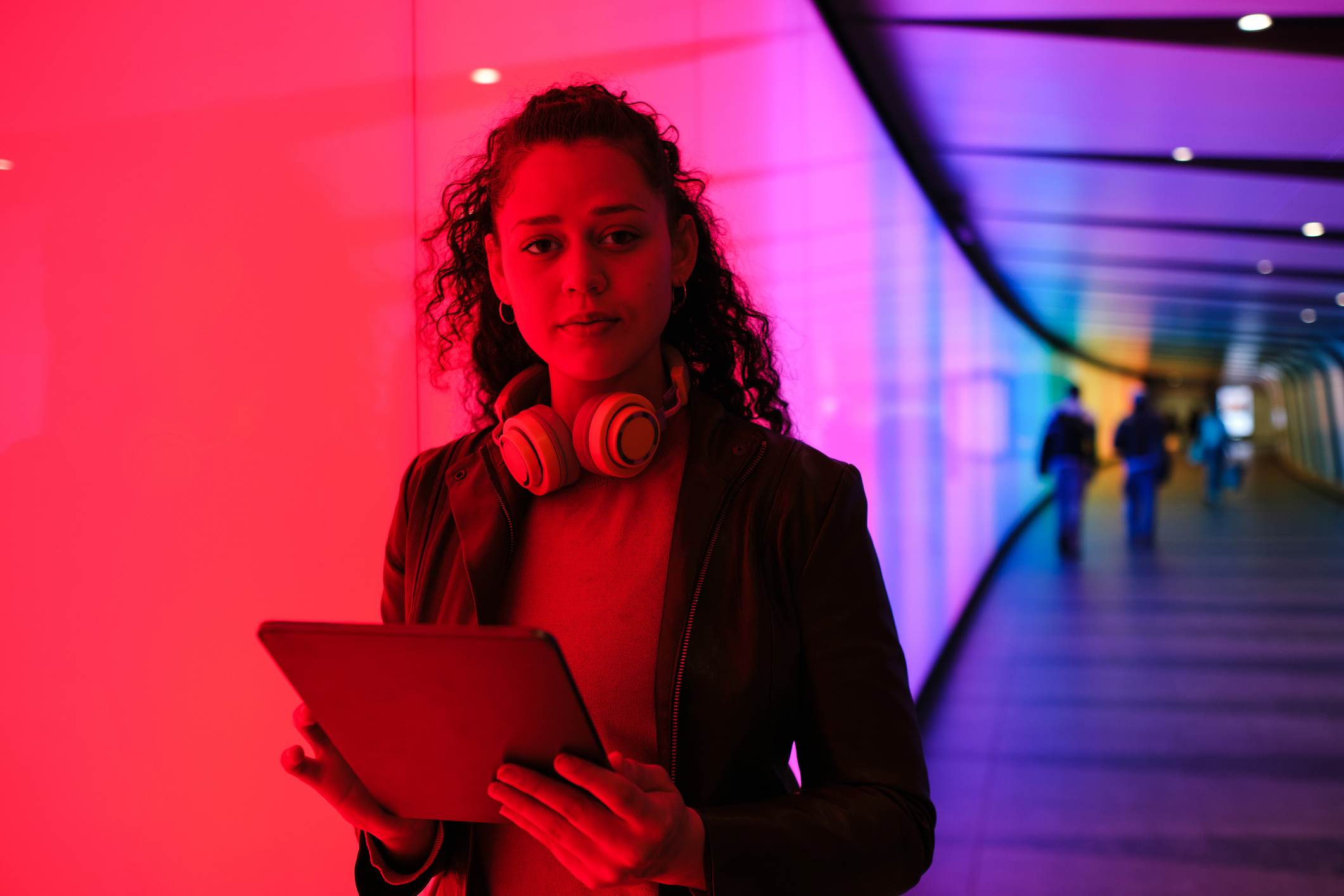 An influencer stands in a purple light tunnel with headphones and tablet in hand, representing social media data.