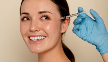 Young Gen Z woman smiling next to a Botox needle, representing Gen Z in the aesthetics industry