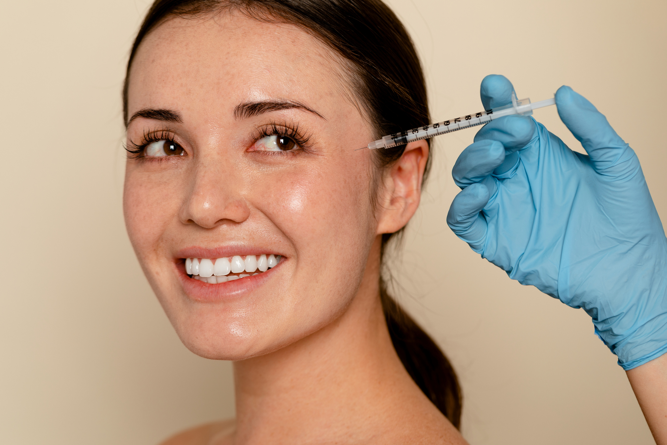 Young Gen Z woman smiling next to a Botox needle, representing Gen Z in the aesthetics industry