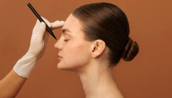 Side profile of a model with a plastic surgeon’s pen poised above her nose, representing plastic surgery industry trends.